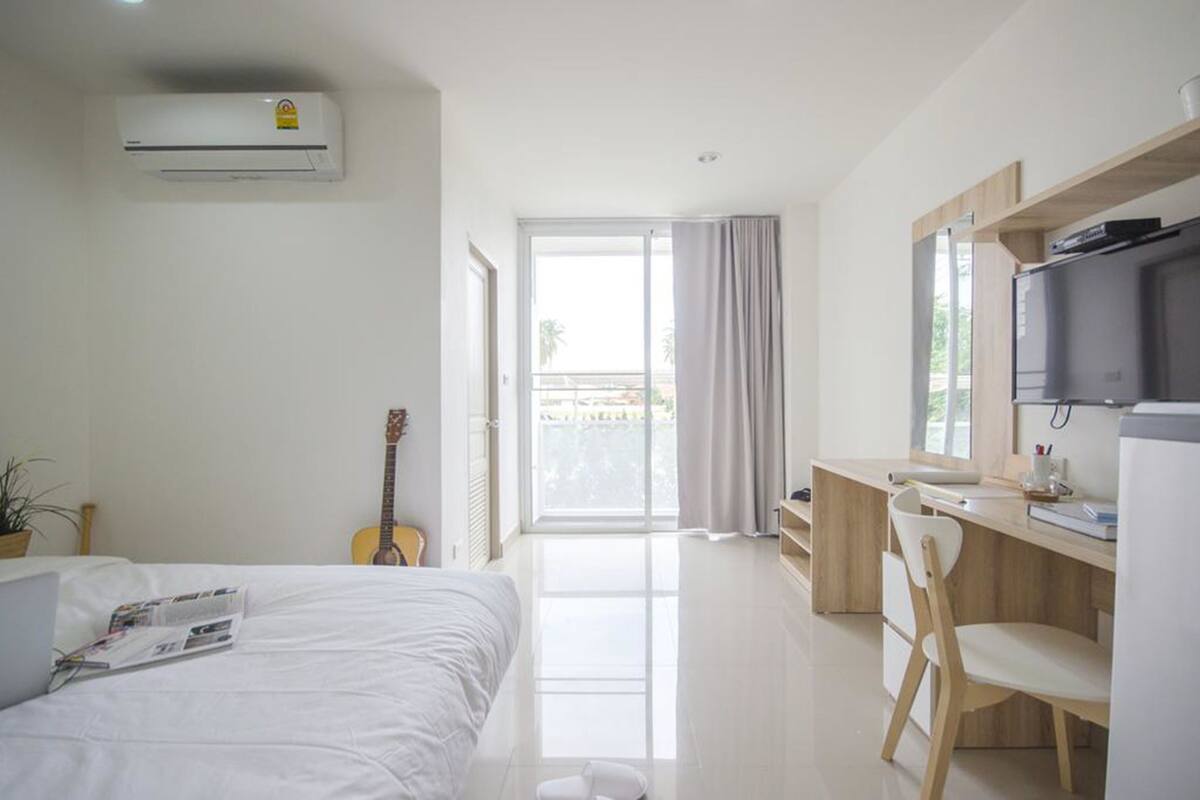 A modern hotel room with a bed, a desk, a television, and a balcony with a view.