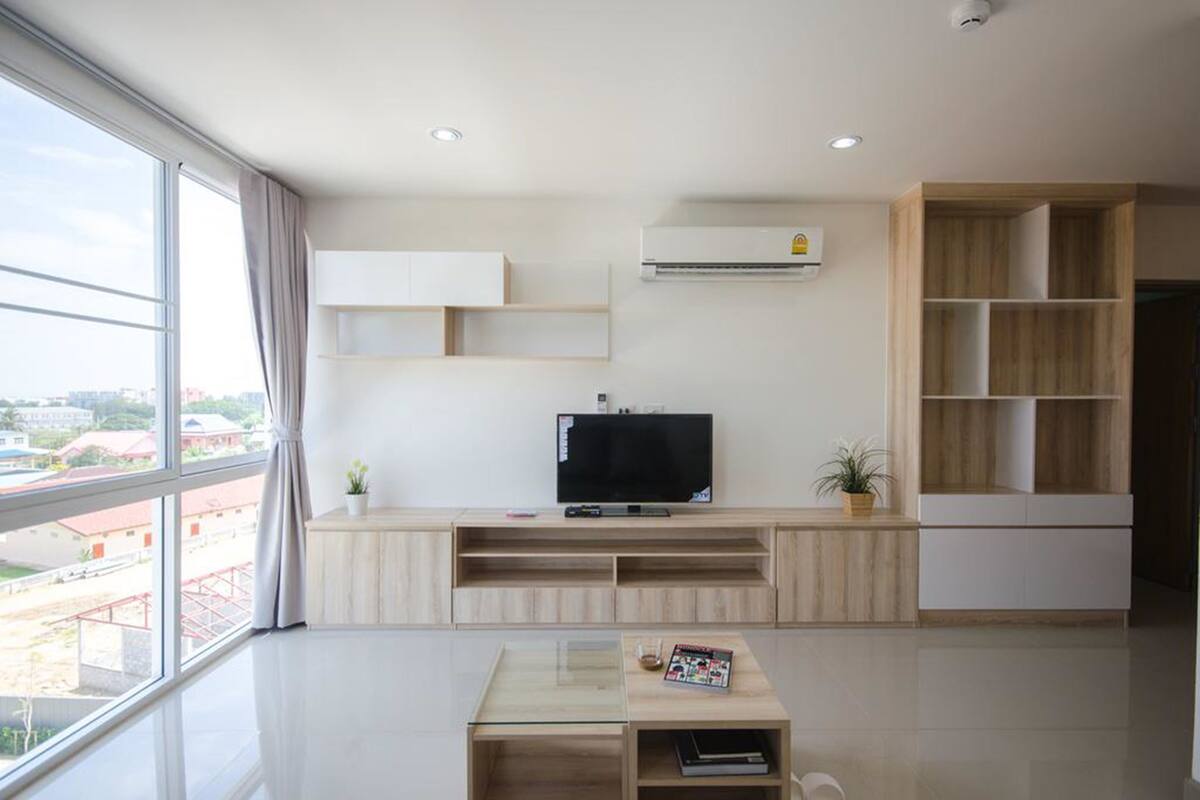 A modern living room with a large window, a flat-screen TV, built-in shelving, and a small table with a magazine.