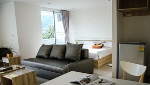 A modern hotel room with a grey sofa, a small wooden side table, a white coffee table, and a bed with a wooden headboard. - Ozone Khaotao (Hua Hin)