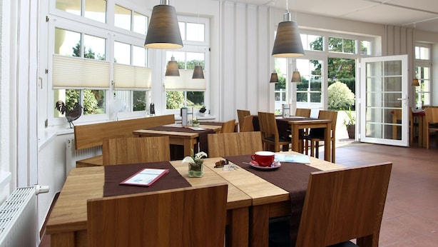 A spacious dining area with wooden tables and chairs, large windows with blinds, and hanging pendant lights.