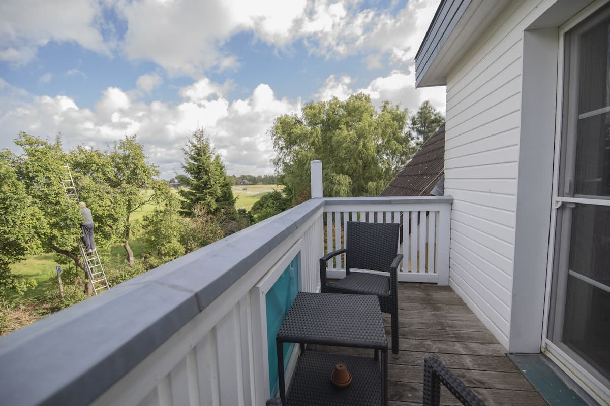 Un espace extérieur abrité doté d’une terrasse en bois, d’une balustrade blanche et offrant une vue sur un paysage verdoyant.