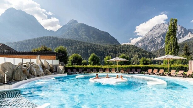 A pool with a mountain backdrop, lounge chairs, and a clear sky. - Hotel Panorama (Scuol)