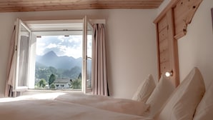 A bedroom with a large bed, a wooden ceiling, and a window with curtains. - Hotel Panorama (Scuol)