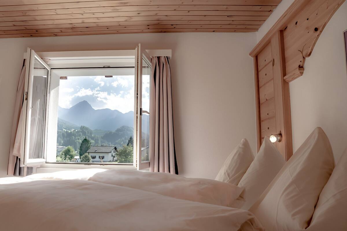 Un dormitorio con una cama grande, techo de madera y ventana con cortinas.