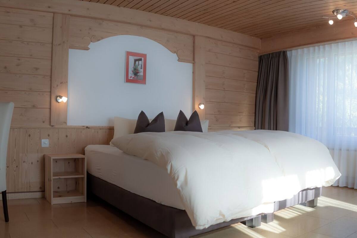 Un dormitorio con una cama grande, una silla, una mesita y un cuadro en la pared.