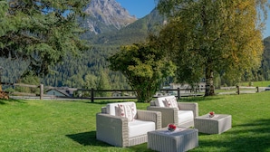 A grassy outdoor seating area with wicker furniture and a view of mountains. - Hotel Panorama (Scuol)