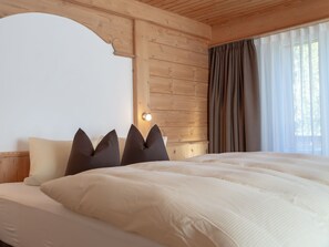 A bedroom with a large bed, wooden headboard, and a window with curtains. - Hotel Panorama (Scuol)