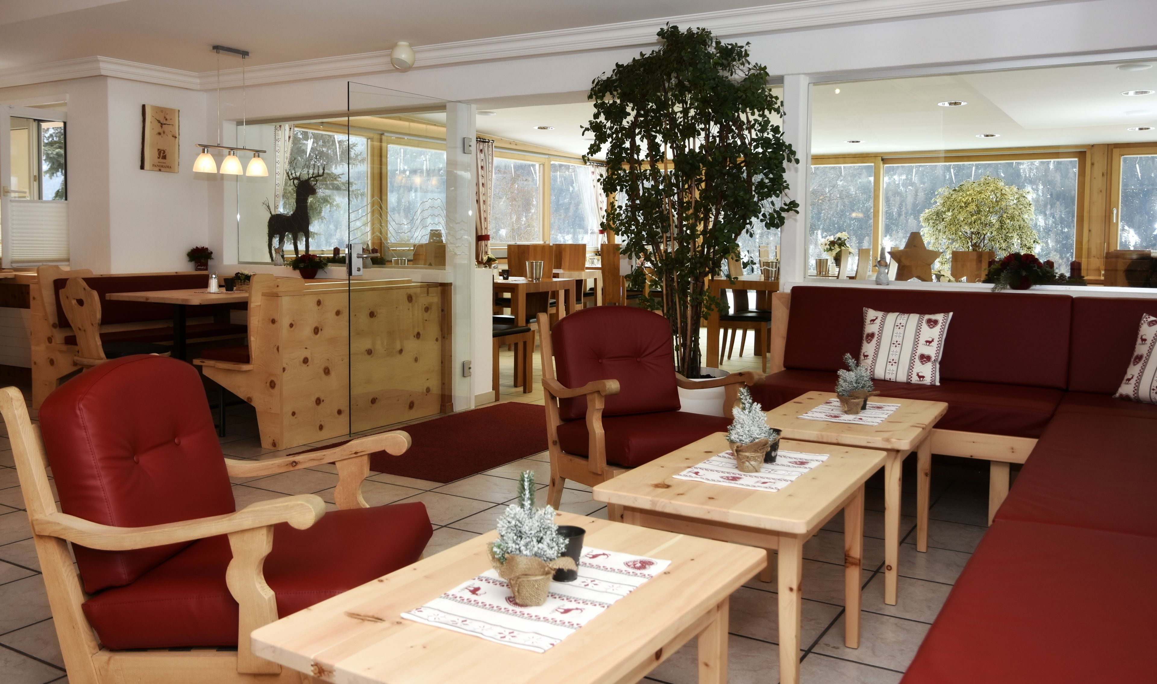 Un restaurant chaleureux, avec des meubles en bois, une grande plante et une vue sur les arbres par les fenêtres.