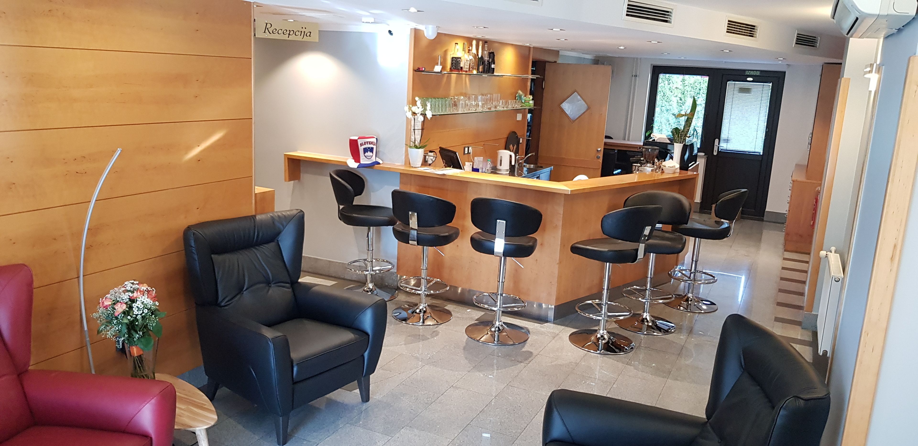 A reception area with a wooden reception desk, black bar stools, and a red chair.