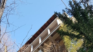 Un edificio con fachada de piedra y techo rojo, rodeado de árboles y terreno rocoso.