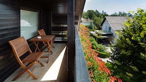 Un balcón con muebles de madera, vista a un jardín con flores rojas y una casa al fondo.