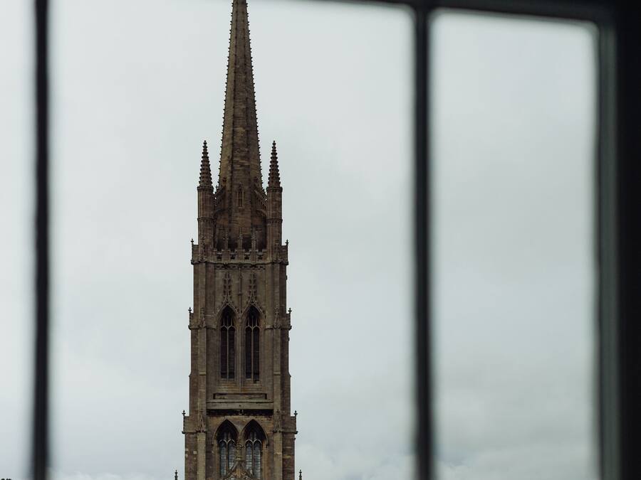 A Gothic-style church with a tall spire, visible through a window with a grid pattern.