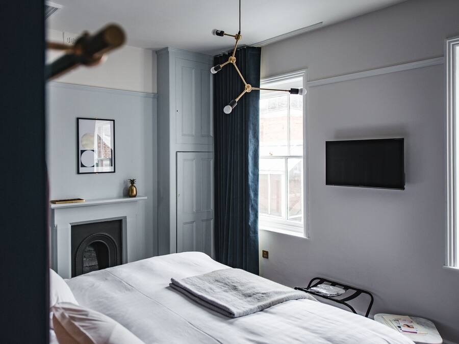 Un dormitorio con una cama, televisión instalada en la pared, chimenea y ventana con cortinas.