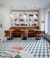 Un interior moderno con un sofá marrón, sillas de madera, piso estampado y una estantería con libros y objetos decorativos.