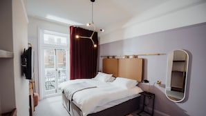 Une chambre à coucher moderne avec un grand lit, une table de chevet, un miroir et une vue sur l’extérieur.