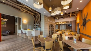 A restaurant with wooden tables and chairs, a bar area, and a wall with a large sun-like design. - Hotel Sole (Maiori)