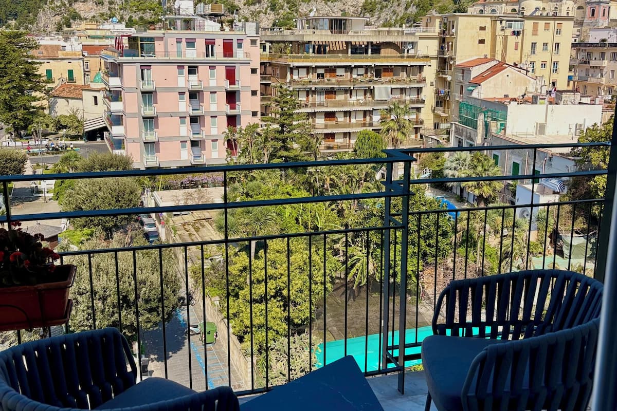 Un balcon avec deux chaises et une table, donnant sur une colline parsemée de bâtiments et de verdure.