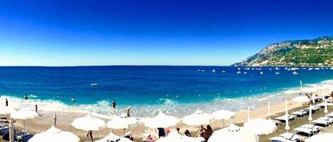 Di pantai, pasir hitam, kursi berjemur, dan payung pantai