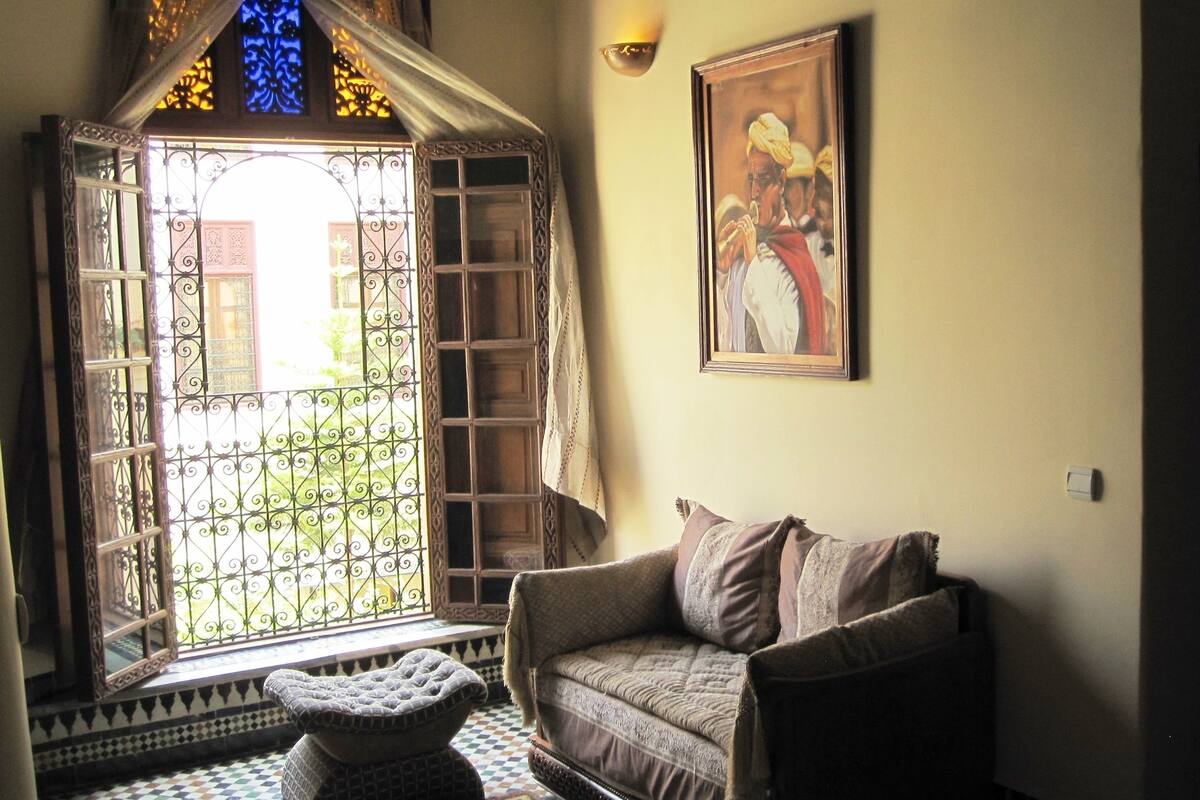 A room with a large window, a cushioned bench, a sofa, and a framed picture on the wall.