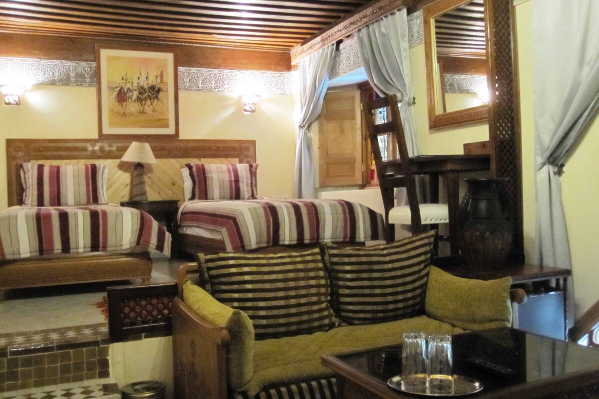A hotel room with two beds, a sofa, a table with glasses, and a painting on the wall.