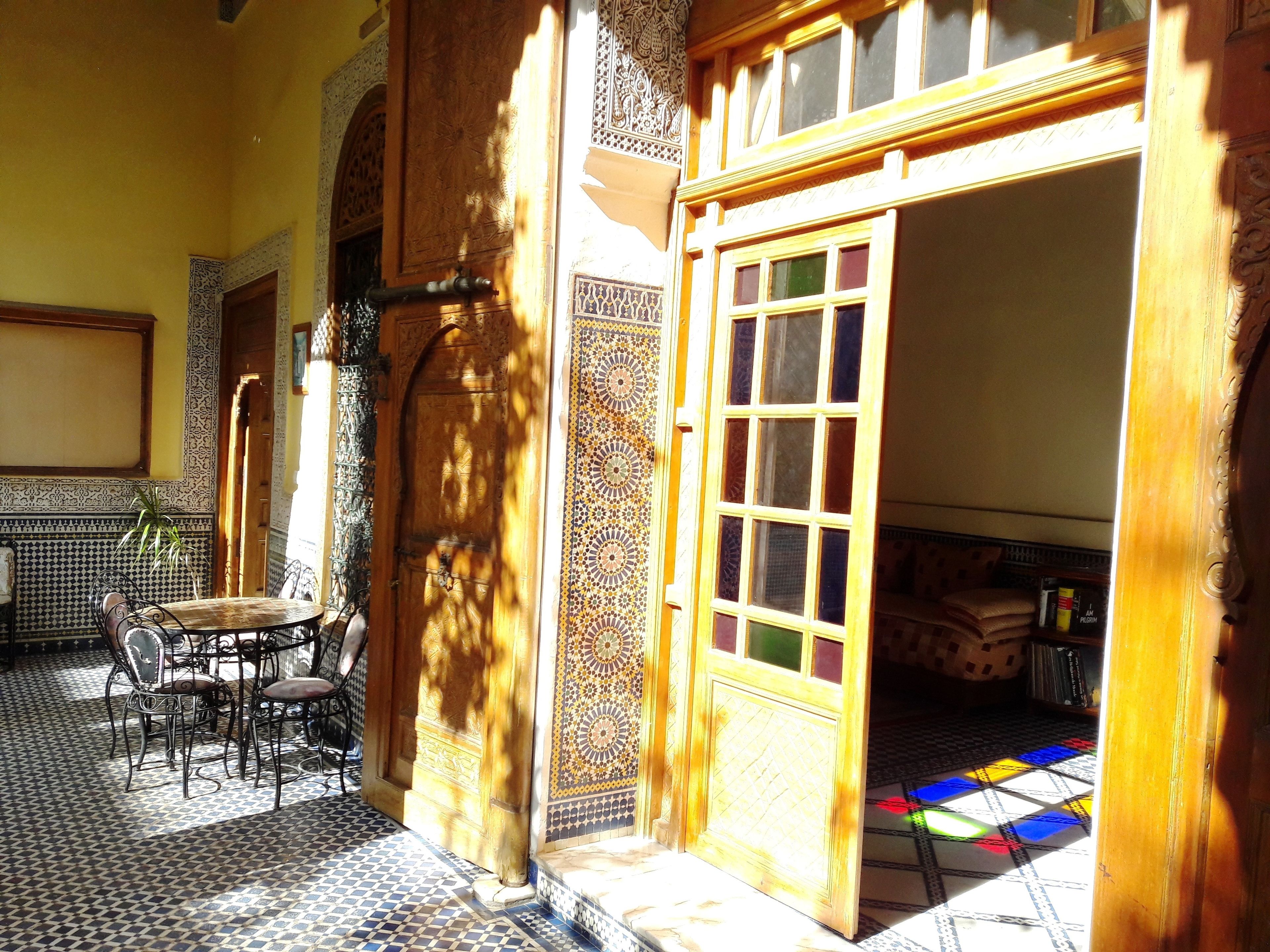 Un interior tradicional marroquí con suelo de baldosas, una puerta de madera y una pequeña mesa con sillas.