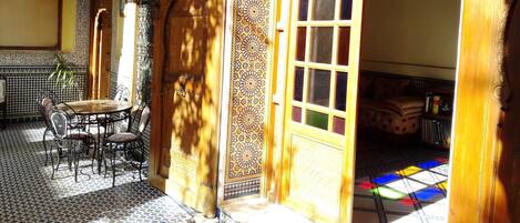 Un interior tradicional marroquí con suelo de baldosas, una puerta de madera y una pequeña mesa con sillas.