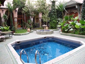 A swimming pool with tiled edges, surrounded by a garden with various plants and a fountain. - Riad Jaouhara (Fes)