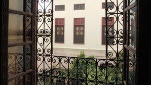 Blick durch schmiedeeiserne Gitter auf ein Gebäude mit zahlreichen Fenstern und einem Balkon.