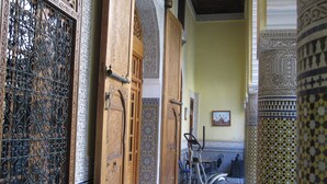 Ein Innenbereich, ein dekorativer Korridor mit verzierten Türen, einem gemusterten Boden und einem stehenden Ergometer.