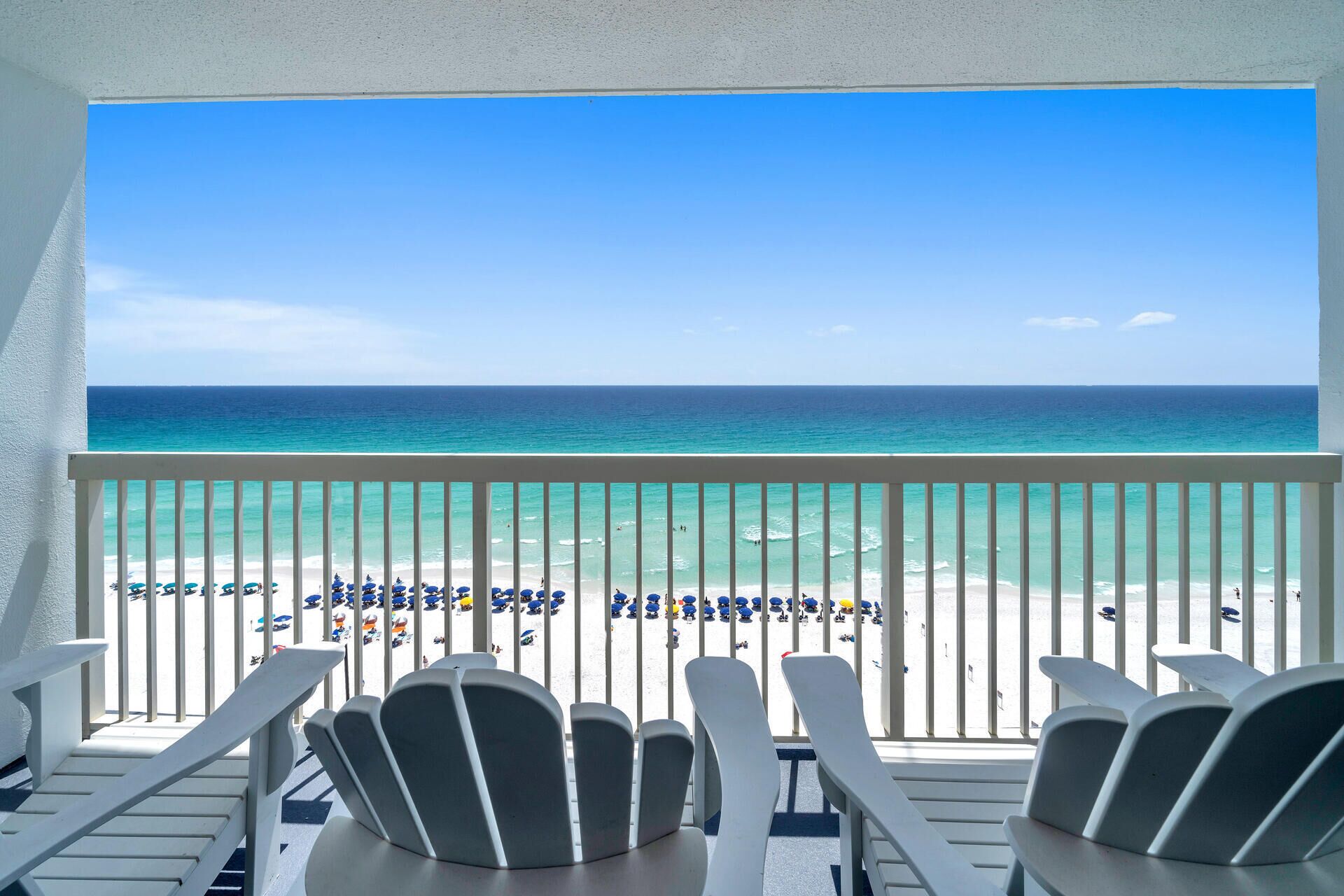 A balcony with white chairs and a view of the beach.