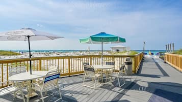 A wooden deck with outdoor seating and umbrellas overlooking a beach.