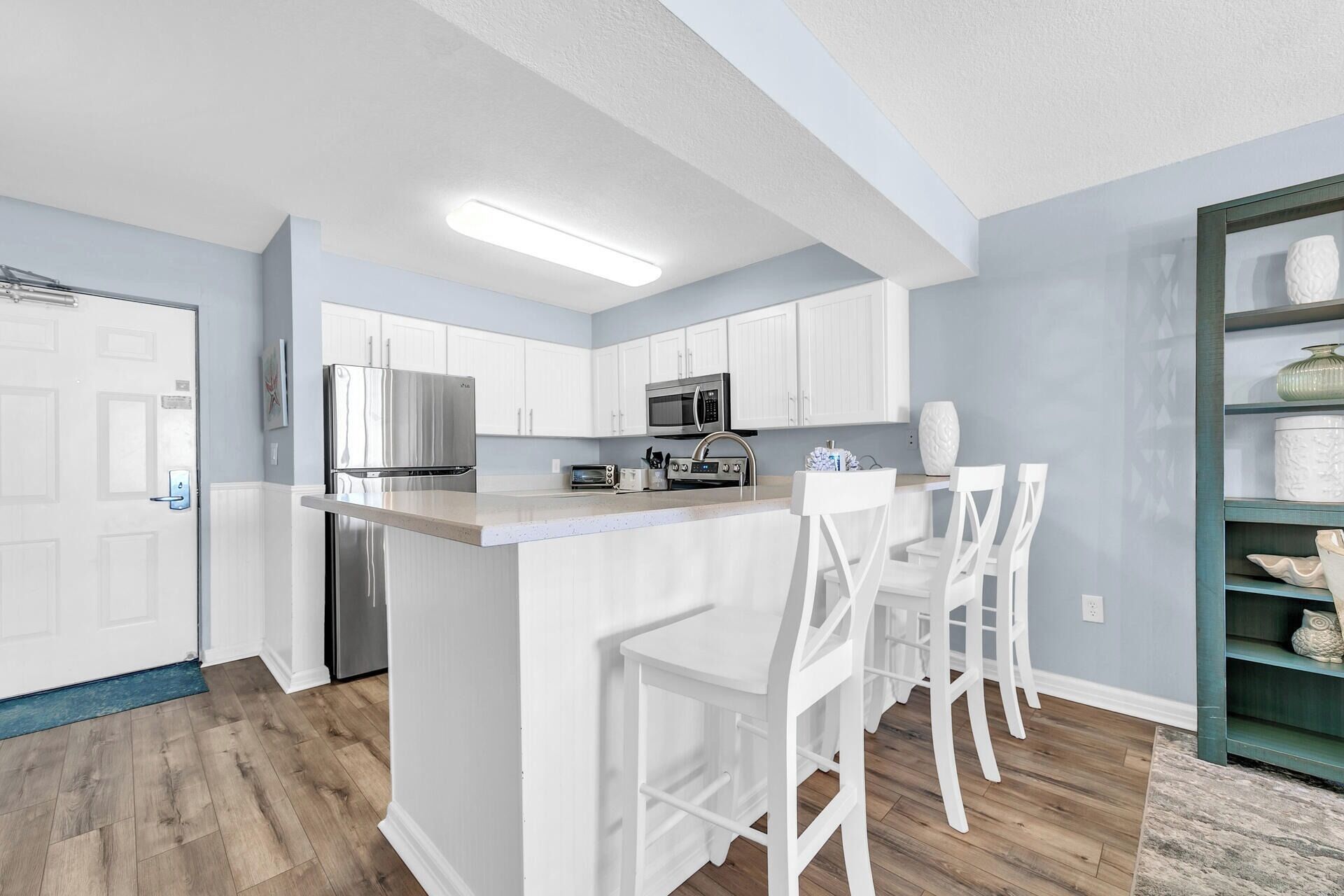A modern kitchen with white cabinetry, stainless steel appliances, and a bar area with white bar stools.