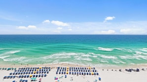 A beach with rows of umbrellas and beach chairs, a clear sky, and the ocean. - Pelican Beach Resort by Colasan (Destin)