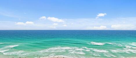 Una playa con hileras de sombrillas y sillas, cielo despejado y el océano.