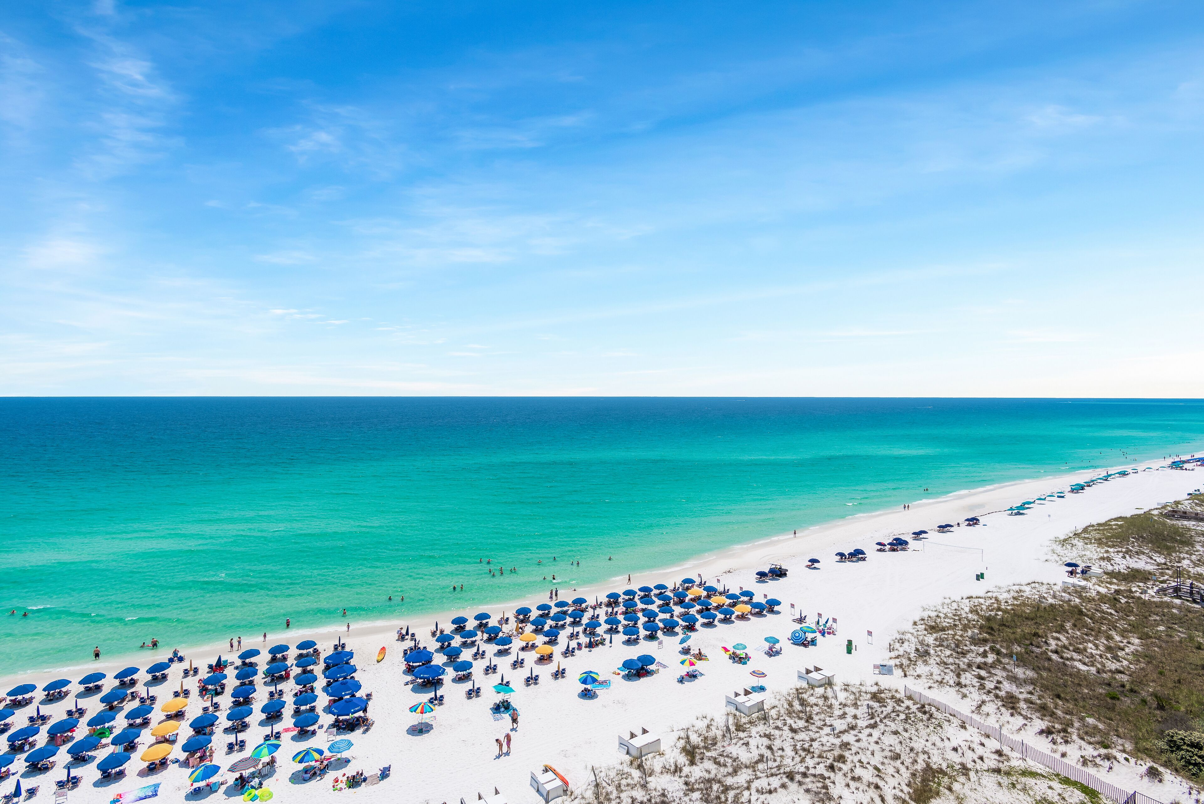 A beach with numerous umbrellas and sun loungers, a sandy shore, and a clear blue sky.