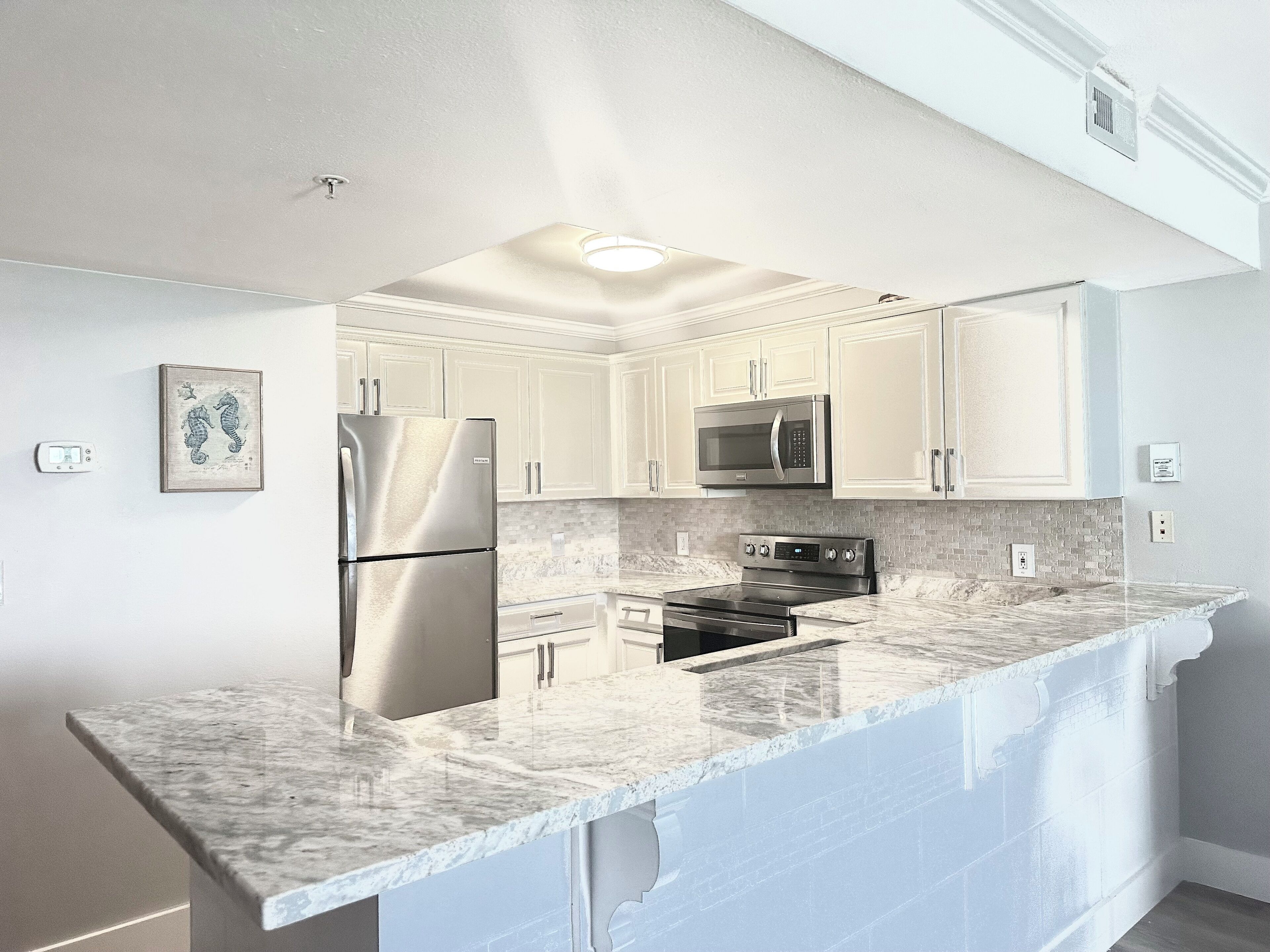 A modern kitchen with white cabinets, stainless steel appliances, and a marble countertop.