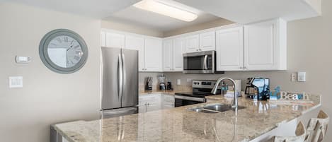 Una cocina moderna con armarios blancos, encimeras de granito, electrodomésticos de acero inoxidable y microondas integrado.