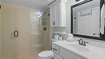 A modern bathroom with a glass shower enclosure, a white toilet, a sink with a mirror, and a towel rack.