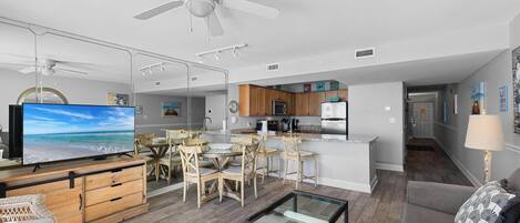 A modern living room with a TV, wooden furniture, a glass coffee table, and a ceiling fan.