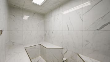 A modern bathroom with white marble tiles, a skylight, and a corner shower area.