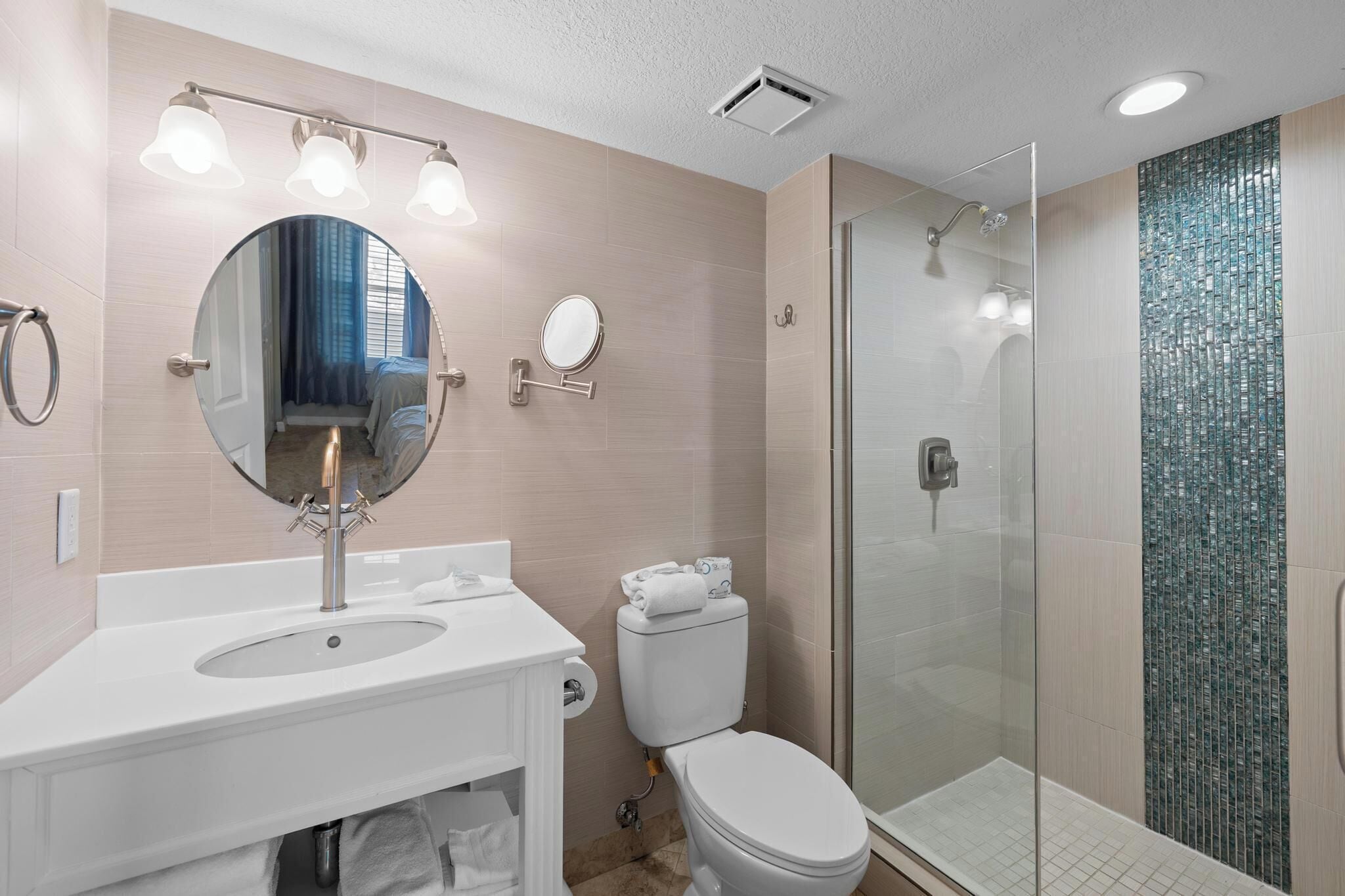 A modern bathroom with a sink, mirror, toilet, and glass-enclosed shower.