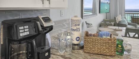 A kitchen with a coffee maker, bottled water, paper towels, and a wicker basket.