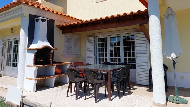 Ein Haus mit einer Terrasse, komplett mit Tisch, Stühlen, einem Grill und einer Pergola.