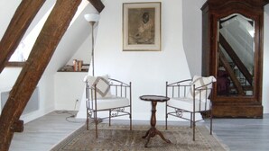 Una habitación con techo alto, vigas de madera a la vista, una pequeña mesa redonda con sillas, un tapete estampado, un cuadro en la pared y un espejo grande.