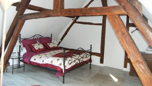 Un dormitorio tipo loft con techo alto, vigas de madera a la vista, estructura de cama metálica y colcha estampada.