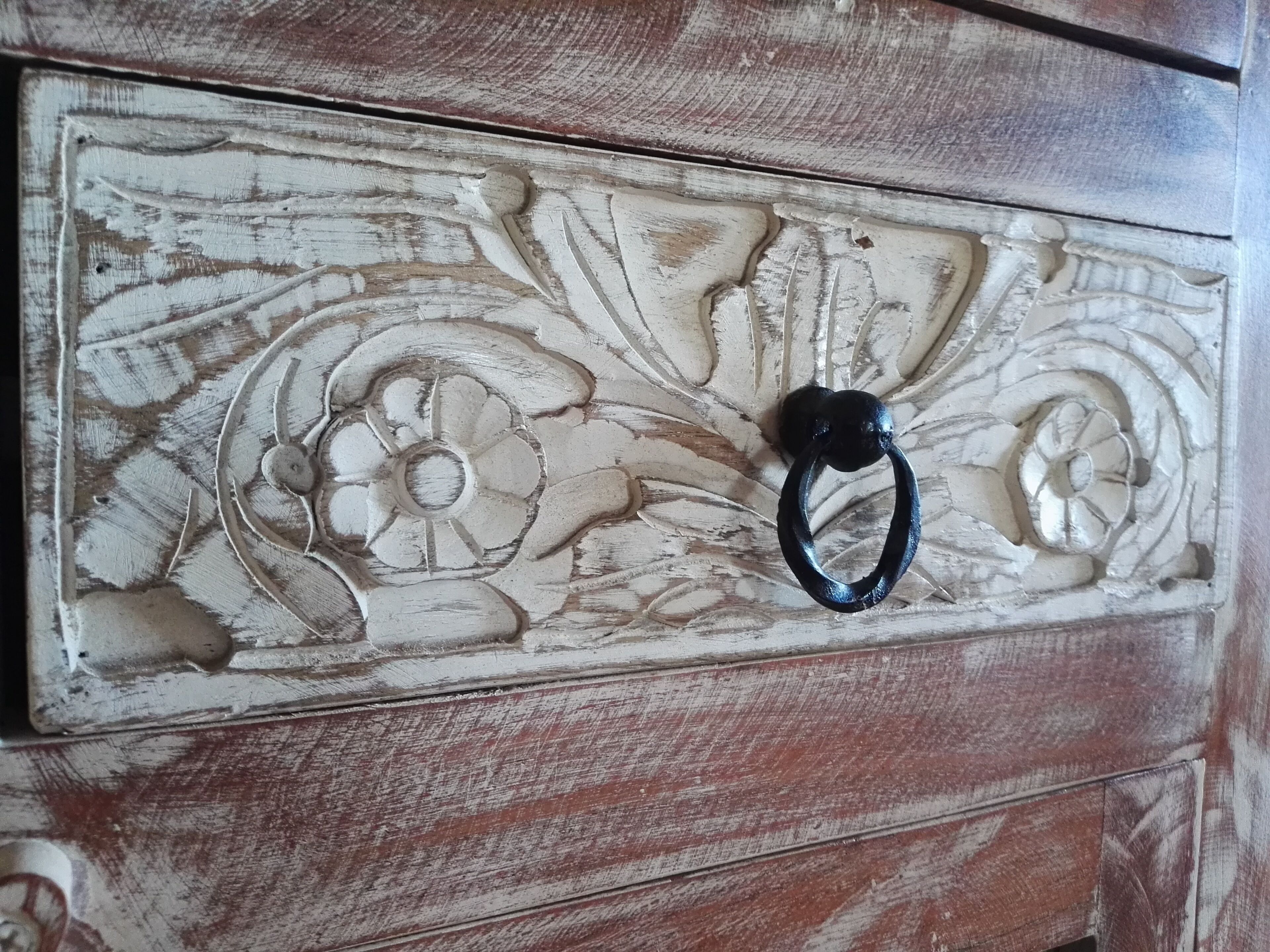 Uma cômoda de madeira com acabamento desgastado e puxador de metal preto.