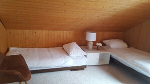 Een knus kamertje met twee eenpersoonsbedden, een nachtkastje met lamp en een tafeltje met een bloevas.