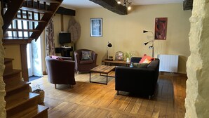 A cozy living room with wooden flooring, a staircase, a sofa, a coffee table, and a bookshelf. - quiet cottage, near Poligny and Arbois, vineyards, lakes, waterfalls, hiking (Villerserine)