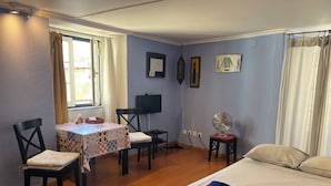 Een kamer met een bed, een tafel met stoelen, een televisie en een ventilator.