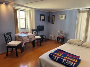 Une chambre avec un lit, une table et des chaises, une télévision et un ventilateur.